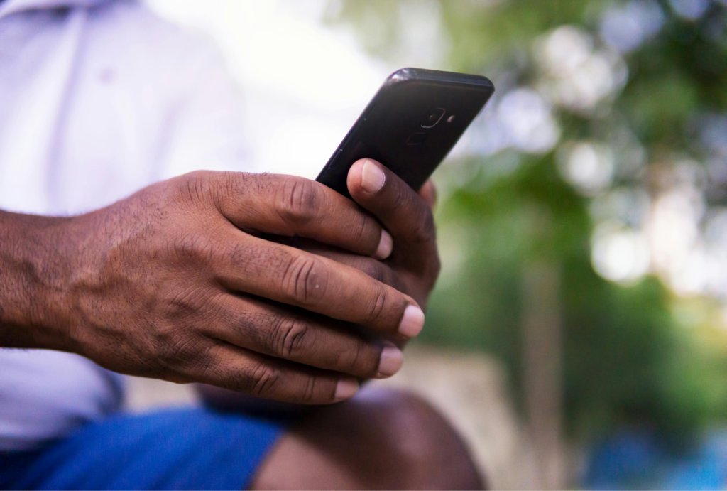 Close-up of hands holding a smartphone outdoors, with a blurred green background.