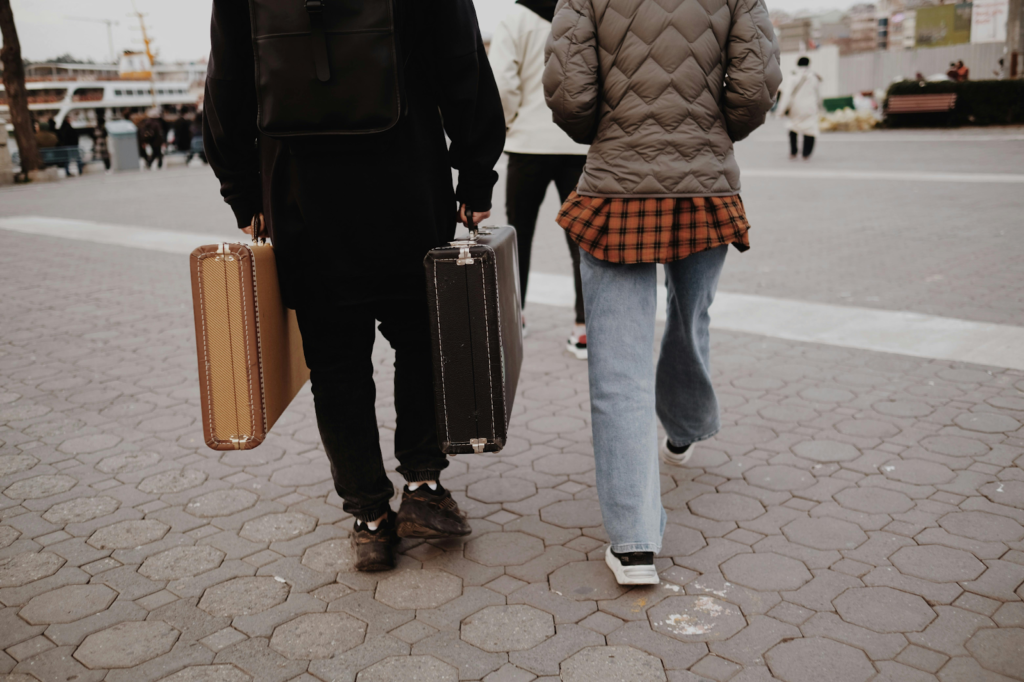 Two people walk on a city sidewalk carrying vintage suitcases.