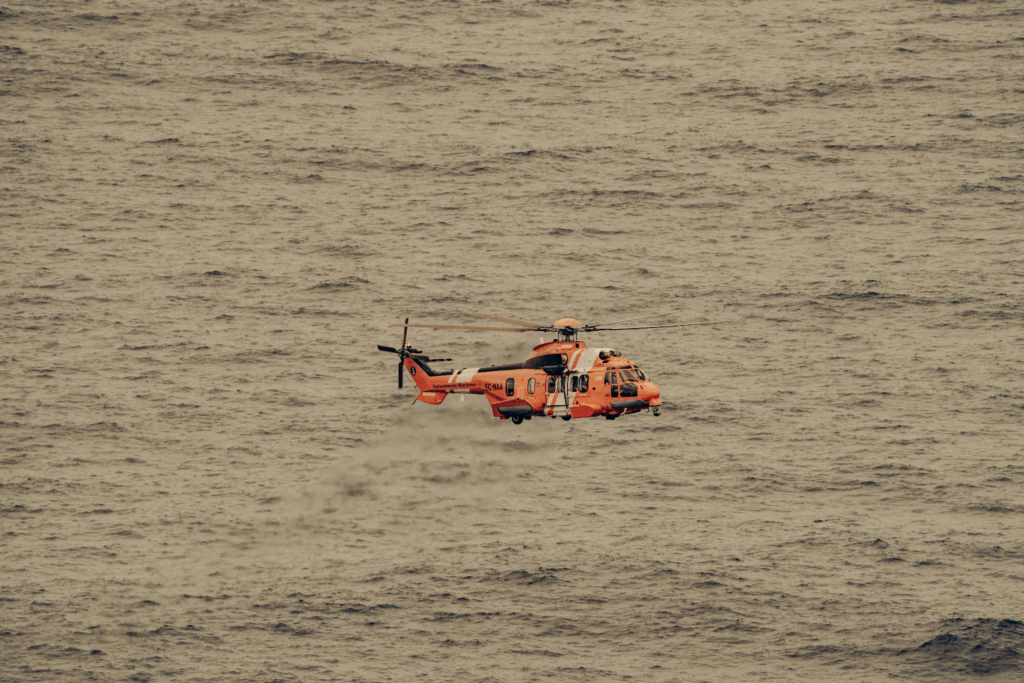 Orange search and rescue helicopter flies low over open sea.