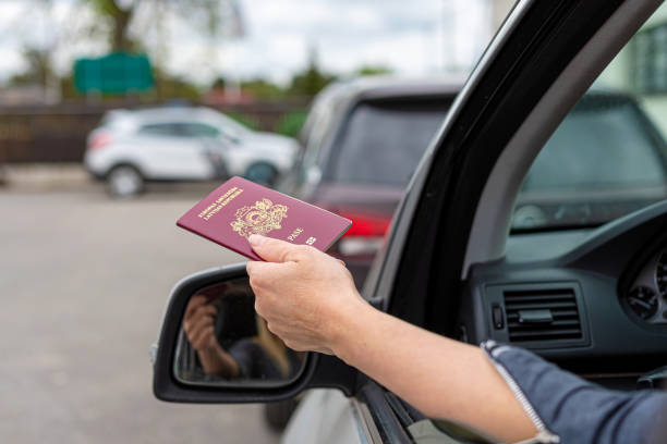 Person holding passport out of car window, likely at border control checkpoint