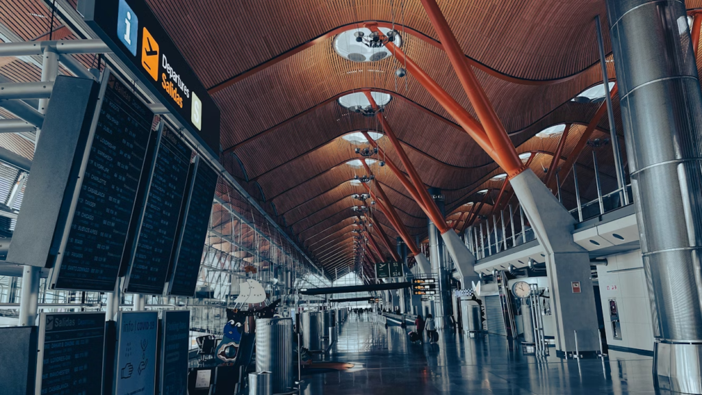 Airport departures terminal with flight information boards and a high curved wooden ceiling.