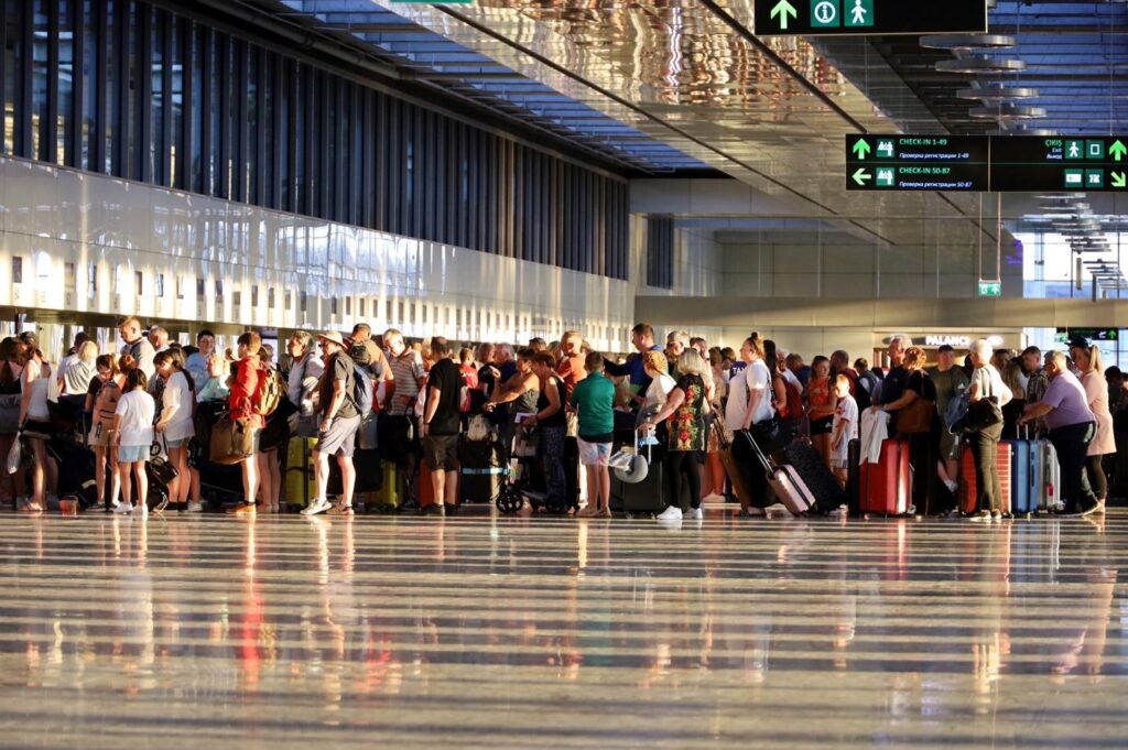 Crowded airport check-in queue of travelers standing with luggage under overhead directional signs.