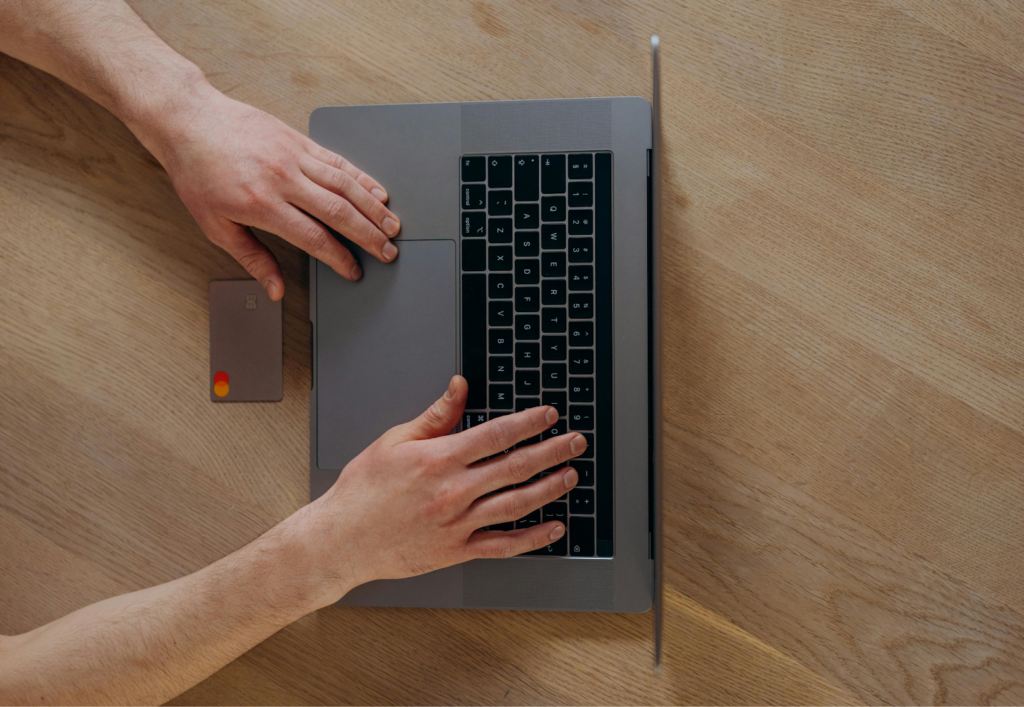 Overhead view of a person typing on a laptop beside a credit card on a wooden desk.