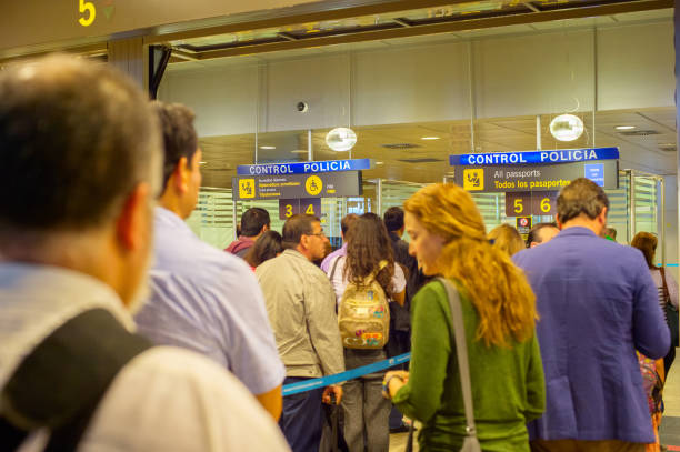 Passengers line up at airport passport control counters with police signage above the booths.