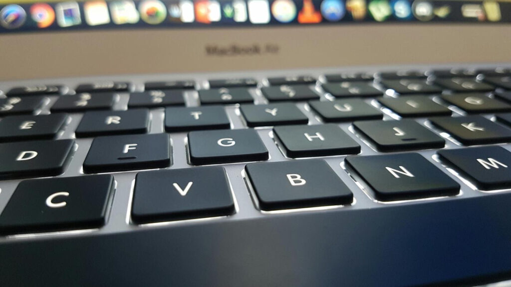 Close-up of a laptop keyboard with black keys and a blurred screen in the background.
