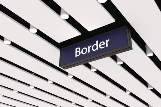 Border control sign hanging from the ceiling in an airport, with modern lighting panels and a patterned ceiling design.