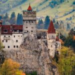 Medieval castle perched on a rocky hill, surrounded by autumn forests and rolling green hills.