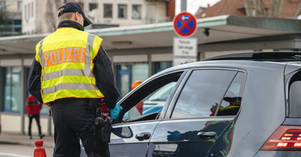 Police officer in high-visibility vest marked “Polizei” speaks to driver during roadside stop