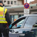 Police officer in high-visibility vest marked “Polizei” speaks to driver during roadside stop