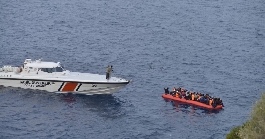 Turkish Coast Guard boat approaches crowded inflatable raft carrying migrants at sea.