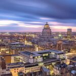 Brussels cityscape at dusk with illuminated buildings, a domed palace, and a glowing Ferris wheel on the skyline.