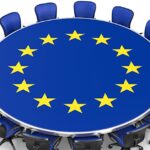 Illustration of a round conference table with the EU flag design and blue chairs arranged around it