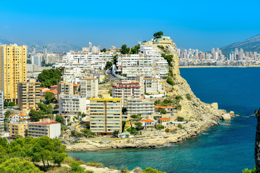 Dense coastal city built on a rocky cliff overlooking a blue sea with high-rise buildings in the background.