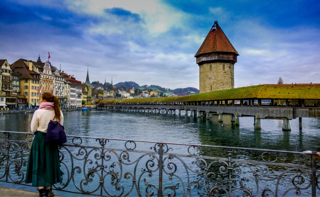 Woman standing by the river looking at Chapel Bridge and the Water Tower in Lucerne, Switzerland.