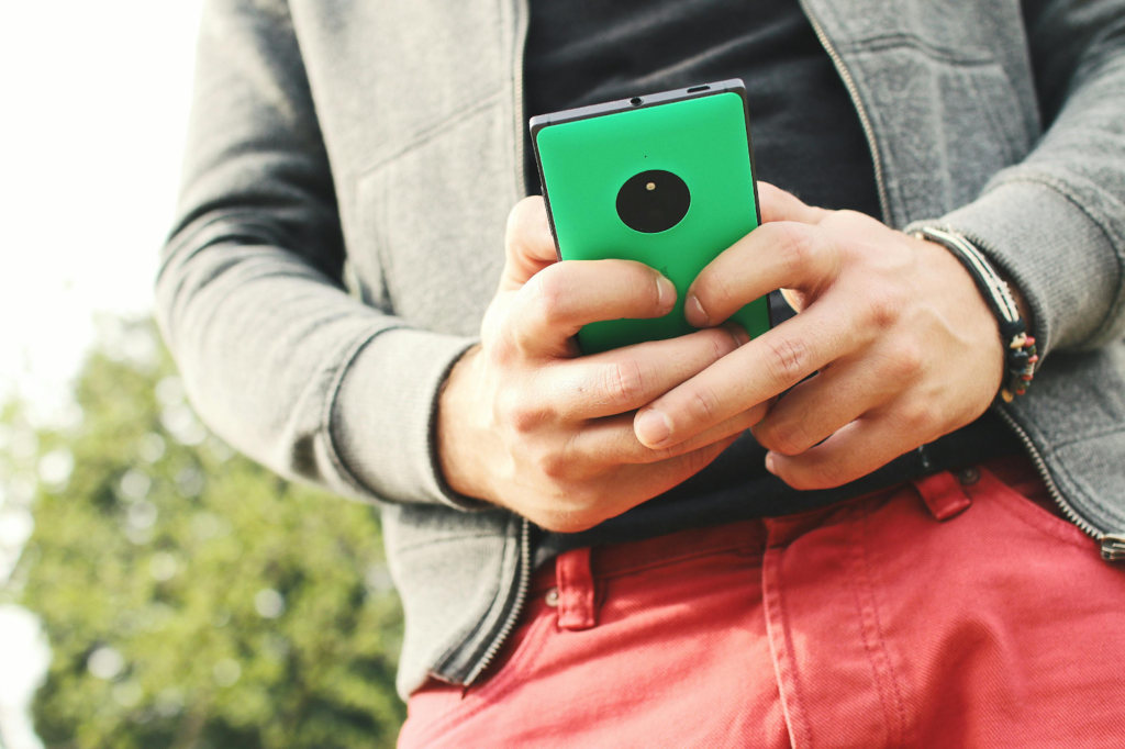 Person holding a green smartphone and typing a message while standing outdoors.
