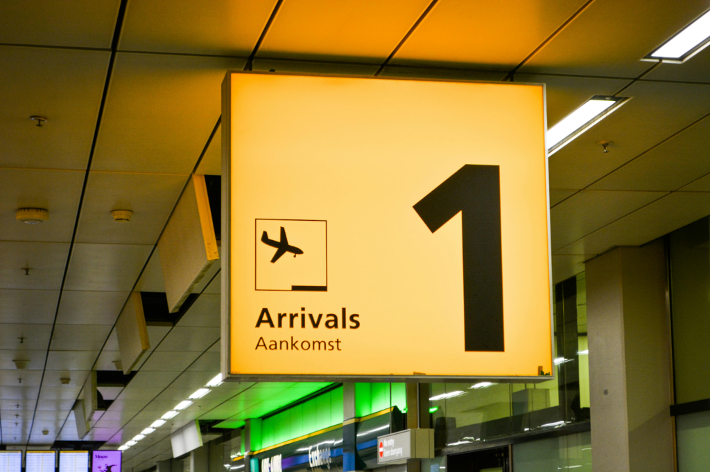 Airport arrivals sign with airplane symbol and large arrow pointing upward inside a terminal corridor.