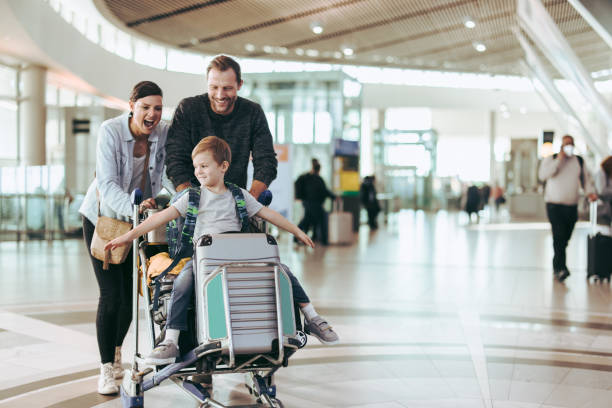 Smiling family pushing child on luggage cart inside airport terminal.