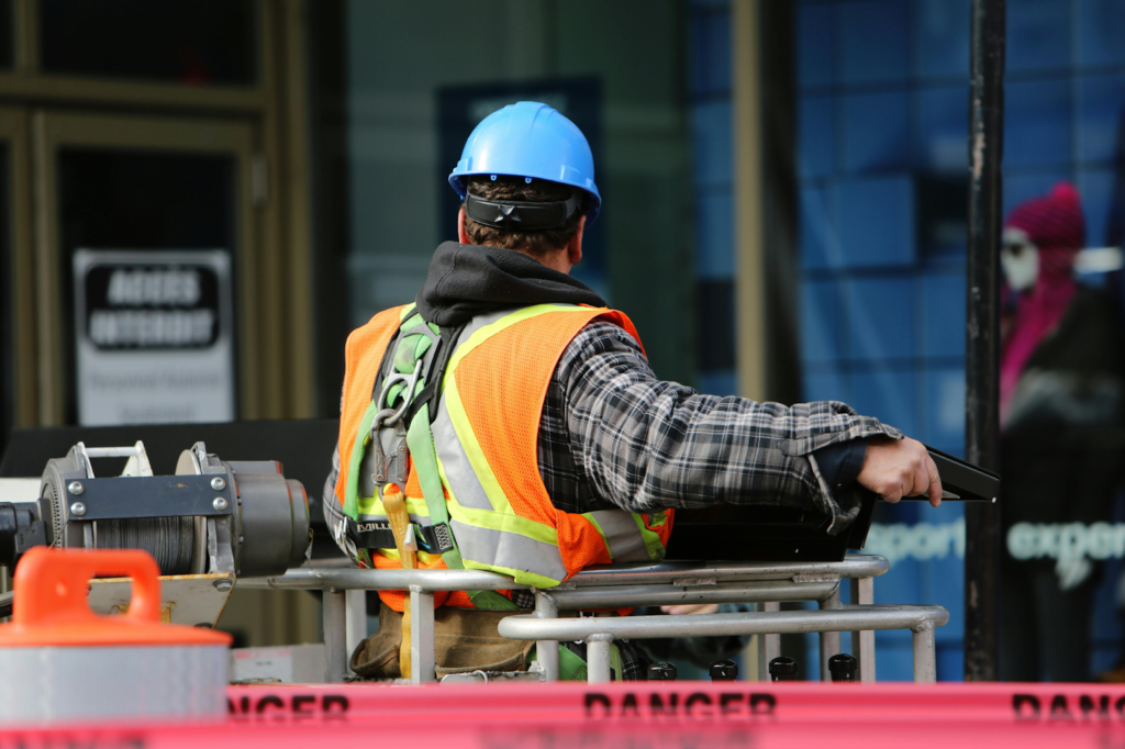 Construction worker wearing a hard hat and safety vest operating a lift at a worksite.