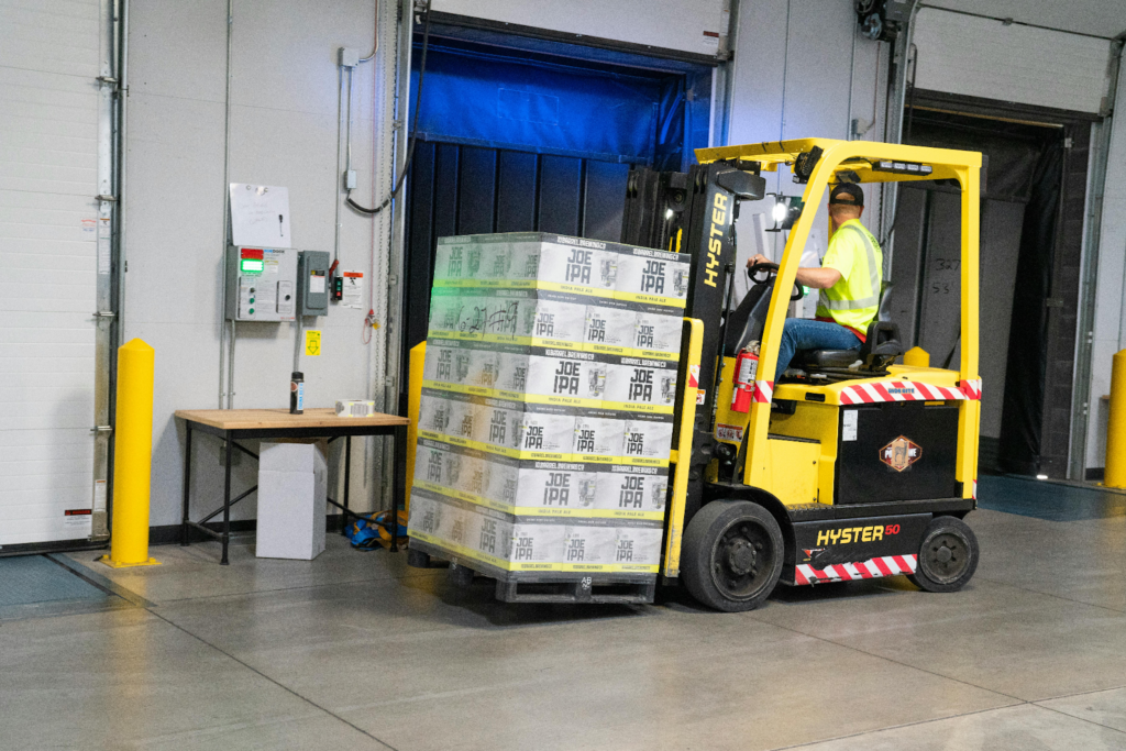 Worker driving a forklift moving a pallet of boxes into a warehouse loading dock.