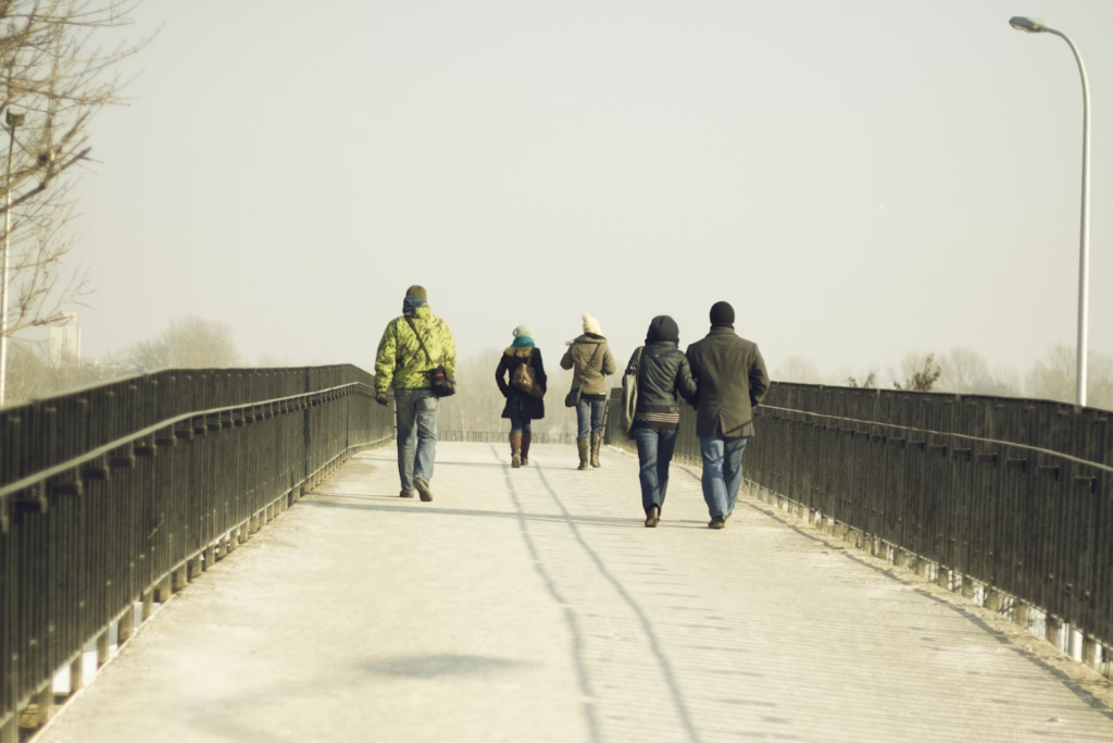 People walk across a pedestrian bridge on a cold day, bundled in coats and hats.