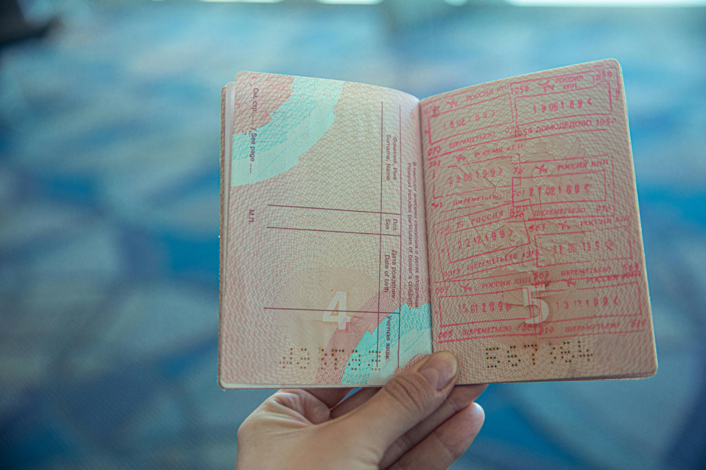 Open passport with multiple stamps held in hand against a blurred airport background.