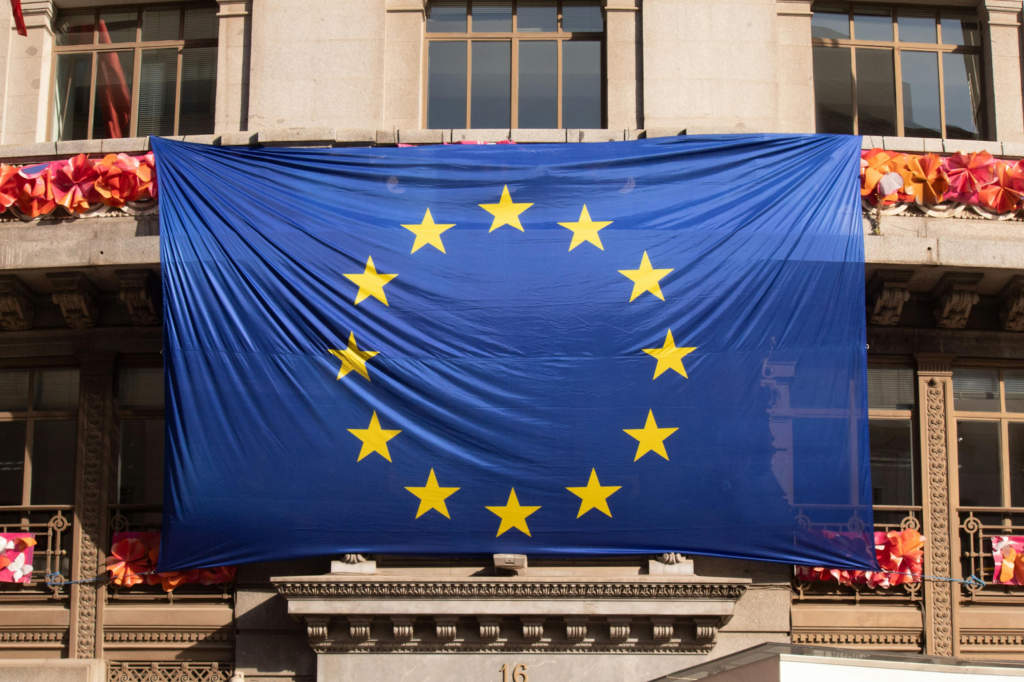 European Union flag hanging on a building facade with windows and decorative elements in the background.