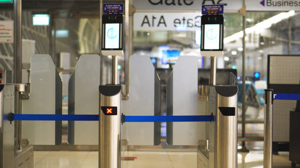 Automated airport boarding gate barriers closed with digital scanners and red access indicators.