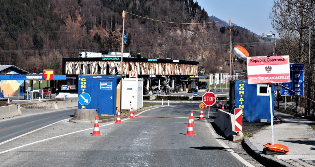 Border checkpoint in Austria with stop sign, traffic cones, and signage marking a controlled road crossing.