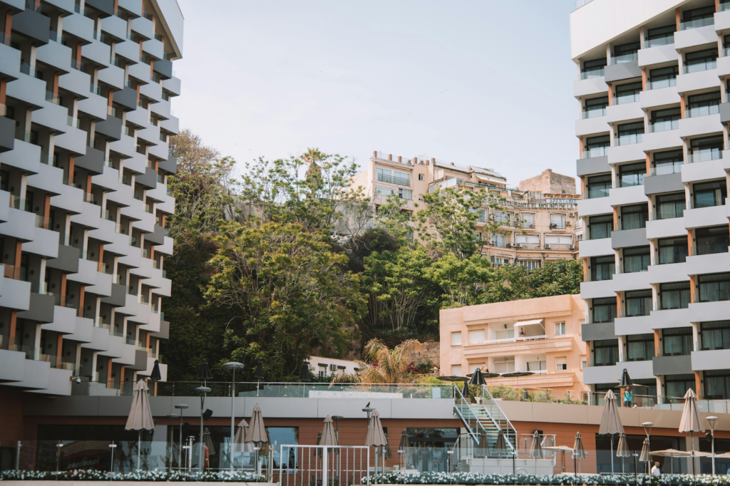 Modern hotel buildings with balconies facing a courtyard and greenery in an urban setting.