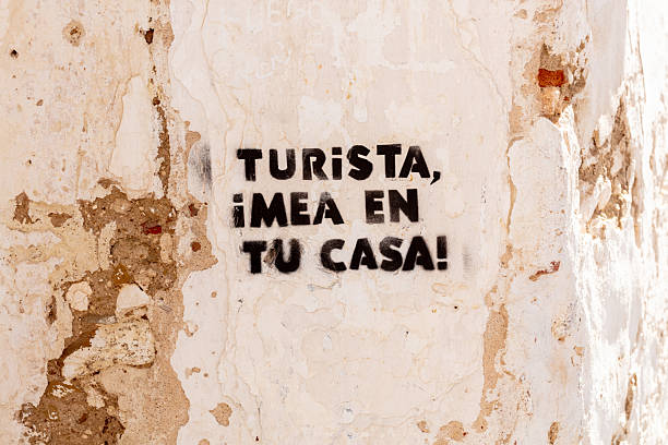 Graffiti reading “Turista, ¡mea en tu casa!” sprayed on a weathered wall.