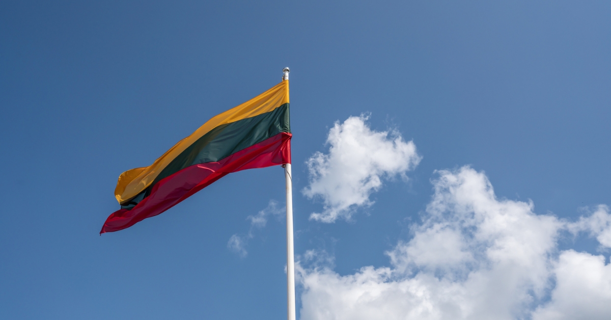 Lithuanian flag waving on a flagpole against a blue sky with clouds.