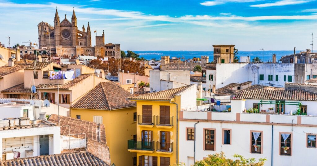 Palma Cathedral rises above colorful Mediterranean rooftops with the sea in the background.