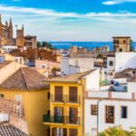 Palma Cathedral rises above colorful Mediterranean rooftops with the sea in the background.