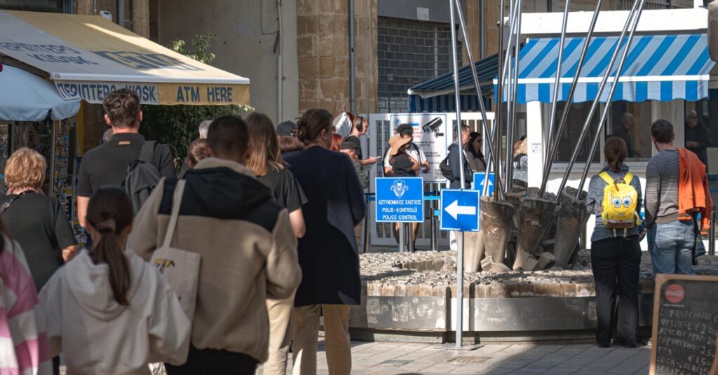 People walking toward a police control checkpoint on a busy street with kiosks and signs