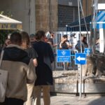 People walking toward a police control checkpoint on a busy street with kiosks and signs