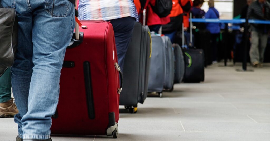 Travelers stand in a queue at airport security with rolling suitcases