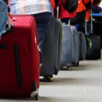 Travelers stand in a queue at airport security with rolling suitcases