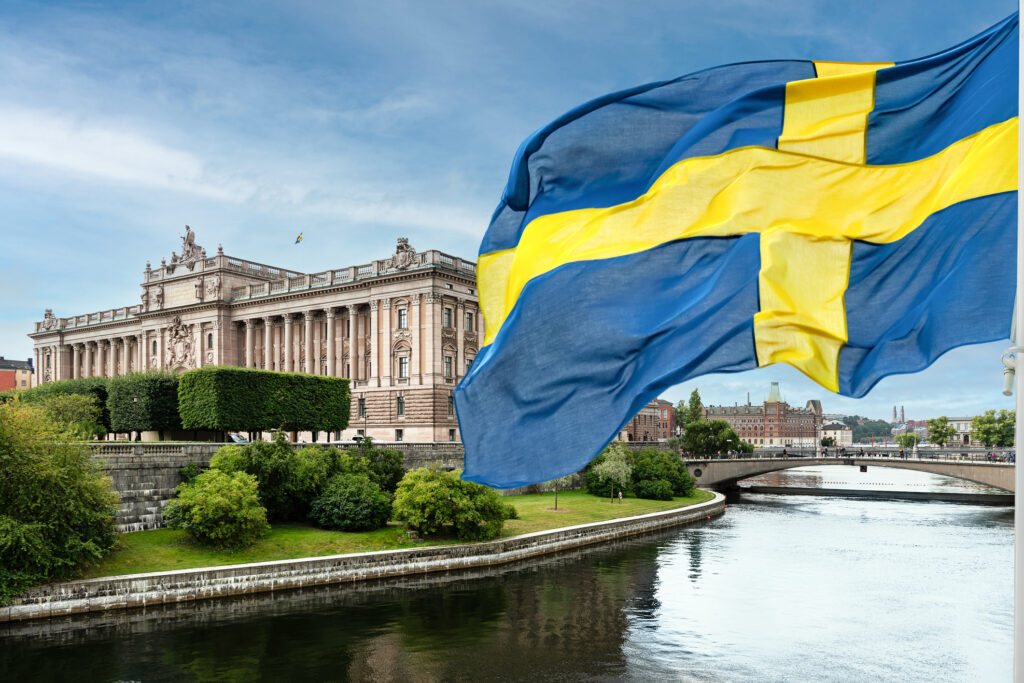 Swedish flag waving over a river with a bridge and historic building in Stockholm