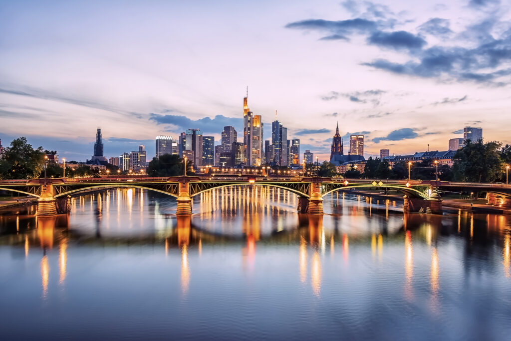 Frankfurt skyline at dusk with illuminated bridge over river and colorful reflections in calm water