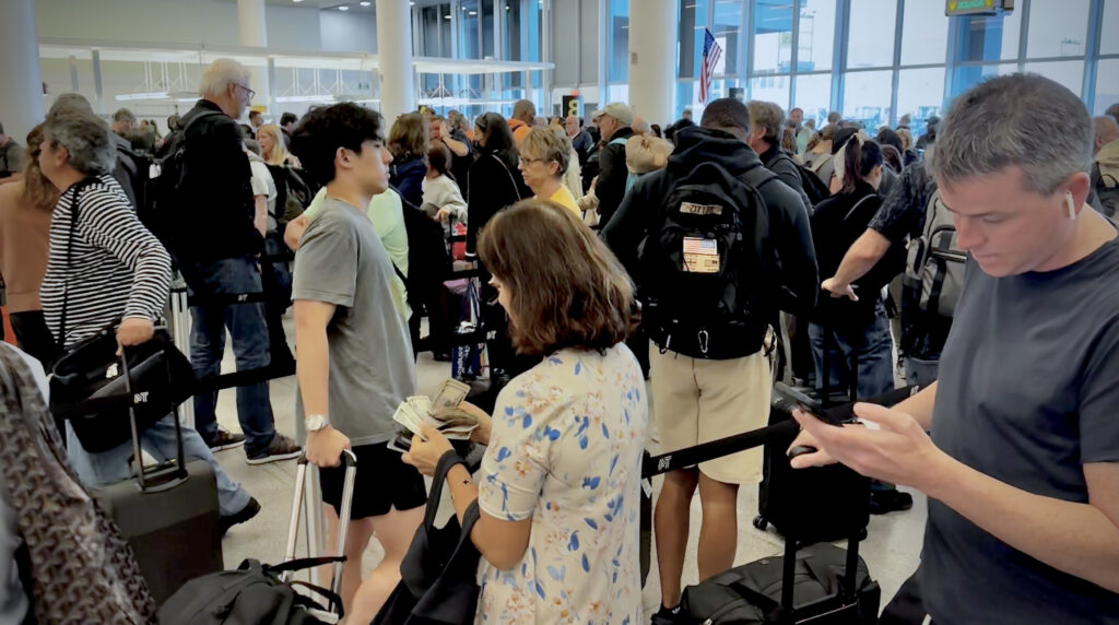 Busy airport security line with travelers holding carry-on luggage and waiting in queue