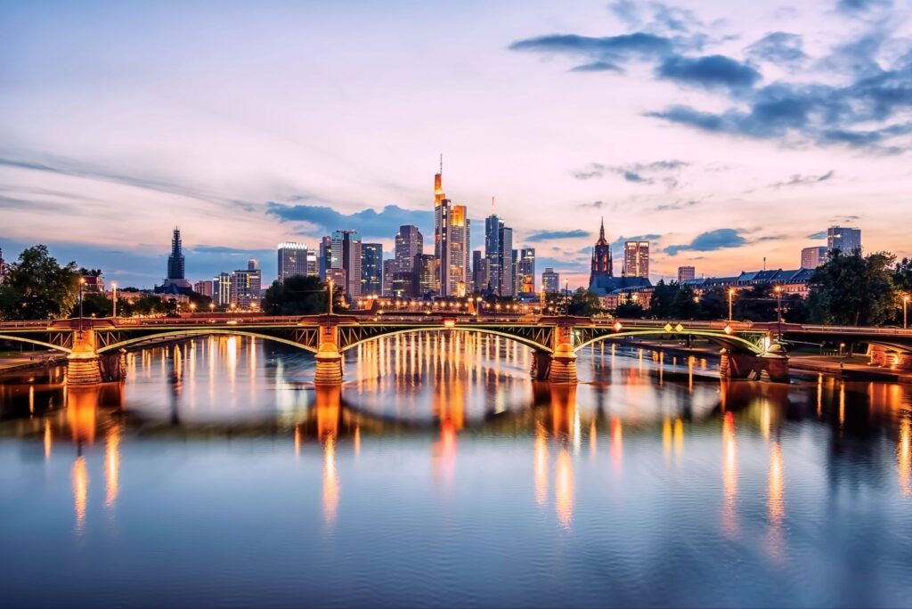City skyline at sunset with a bridge over a river reflecting lights from buildings