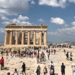Parthenon temple on the Acropolis with crowds of tourists under a bright blue sky and scattered clouds