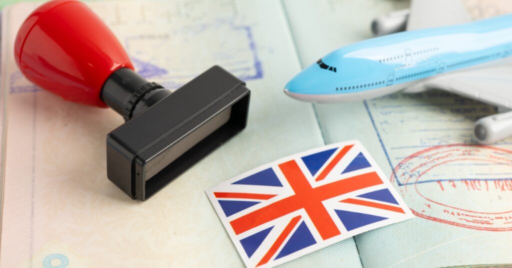 Passport with stamps, rubber stamp, toy airplane, and UK flag sticker on travel documents.