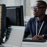 Software developer working at a computer with multiple monitors displaying code in an office setting