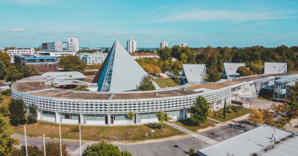 Aerial view of a modern campus with a pyramid-shaped building surrounded by curved structures and trees