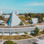 Aerial view of a modern campus with a pyramid-shaped building surrounded by curved structures and trees