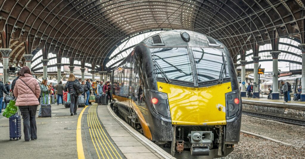 Modern passenger train at a busy station platform under a large arched roof.