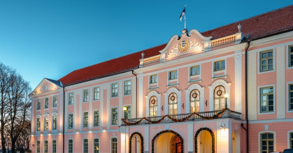 Large pink historic building with holiday lights and arches glowing at dusk under a clear blue sky.