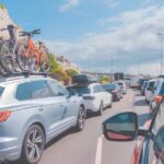 Traffic jam on a motorway with cars lined up and bicycles mounted on a car roof under a blue sky