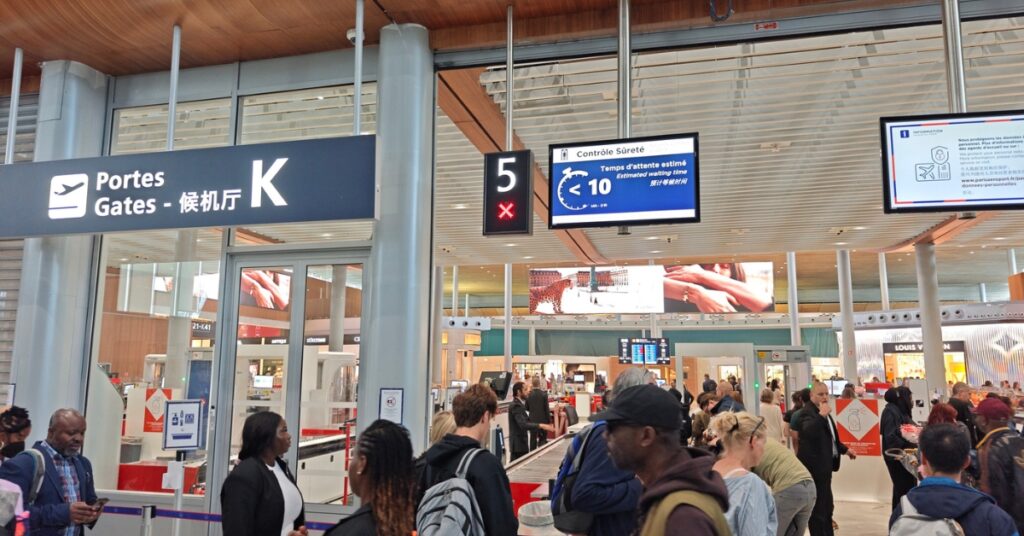 Travelers waiting in line at an airport security checkpoint near Gate K.